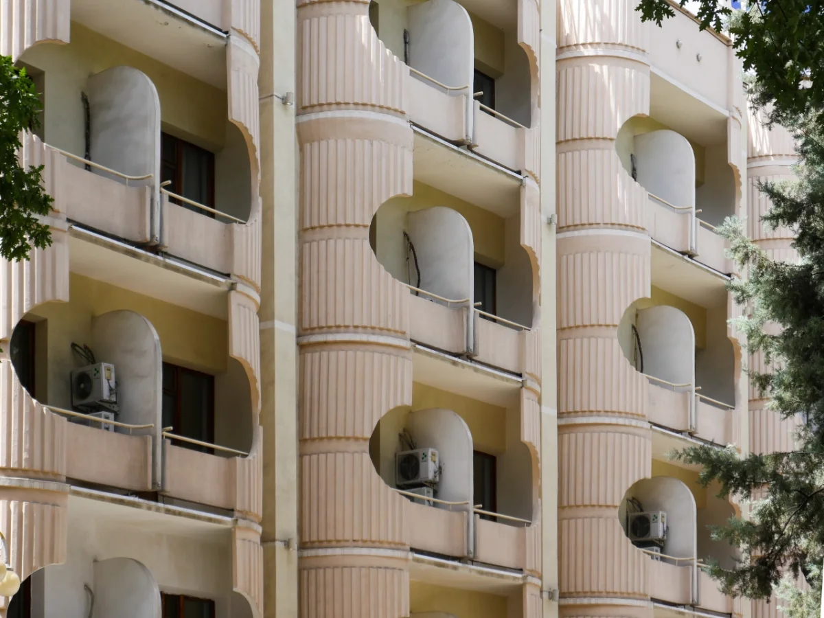 Cream-coloured brutalist apartment building with curved balconies and fluted pilasters, featuring ivy on the right side