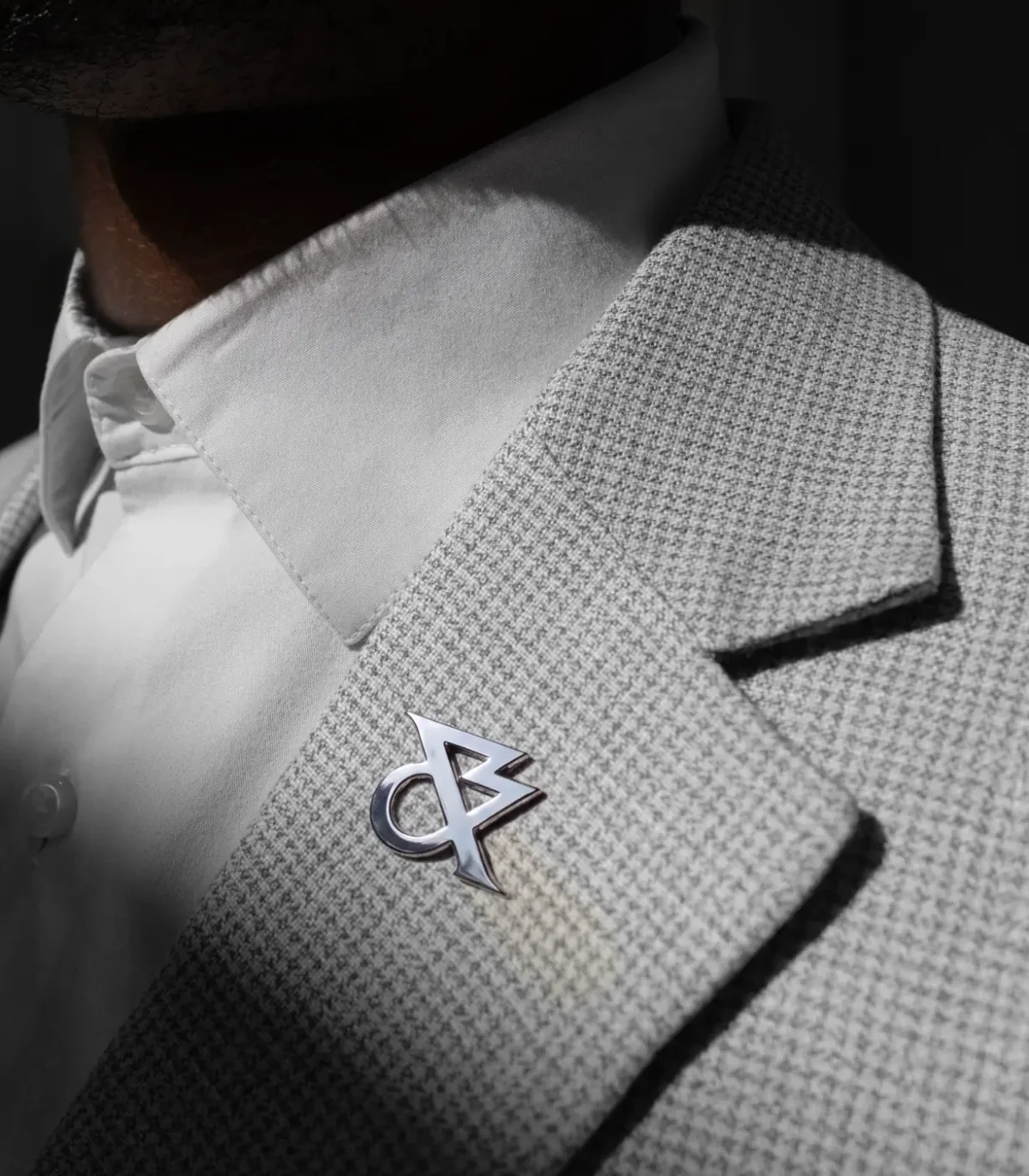 Close-up of a textured grey jacket lapel with White & Case's new angular logo badge in metallic silver, worn with a white shirt