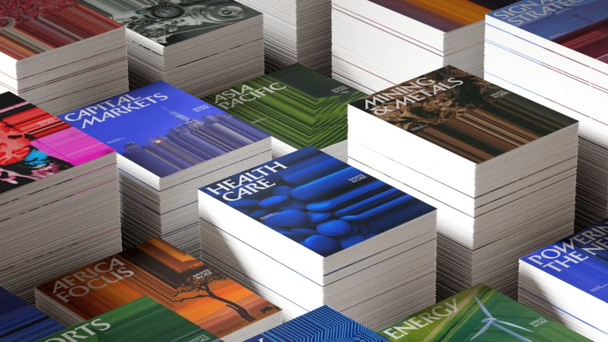 Stacks of printed materials with colorful covers displaying White & Case's new branding, featuring Catalyst Blue and kinetic typography against varied background colours