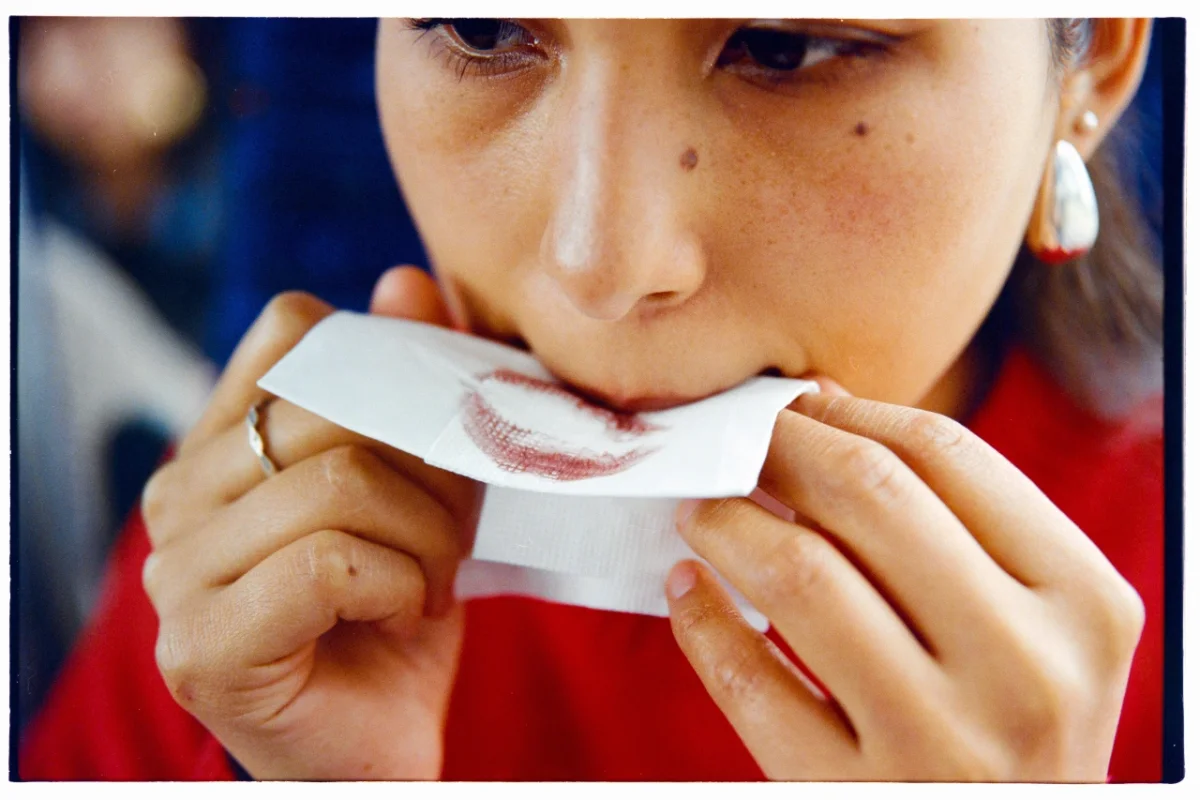 Girl in red shirt examining a lip print or lipstick mark on white paper held between her hands