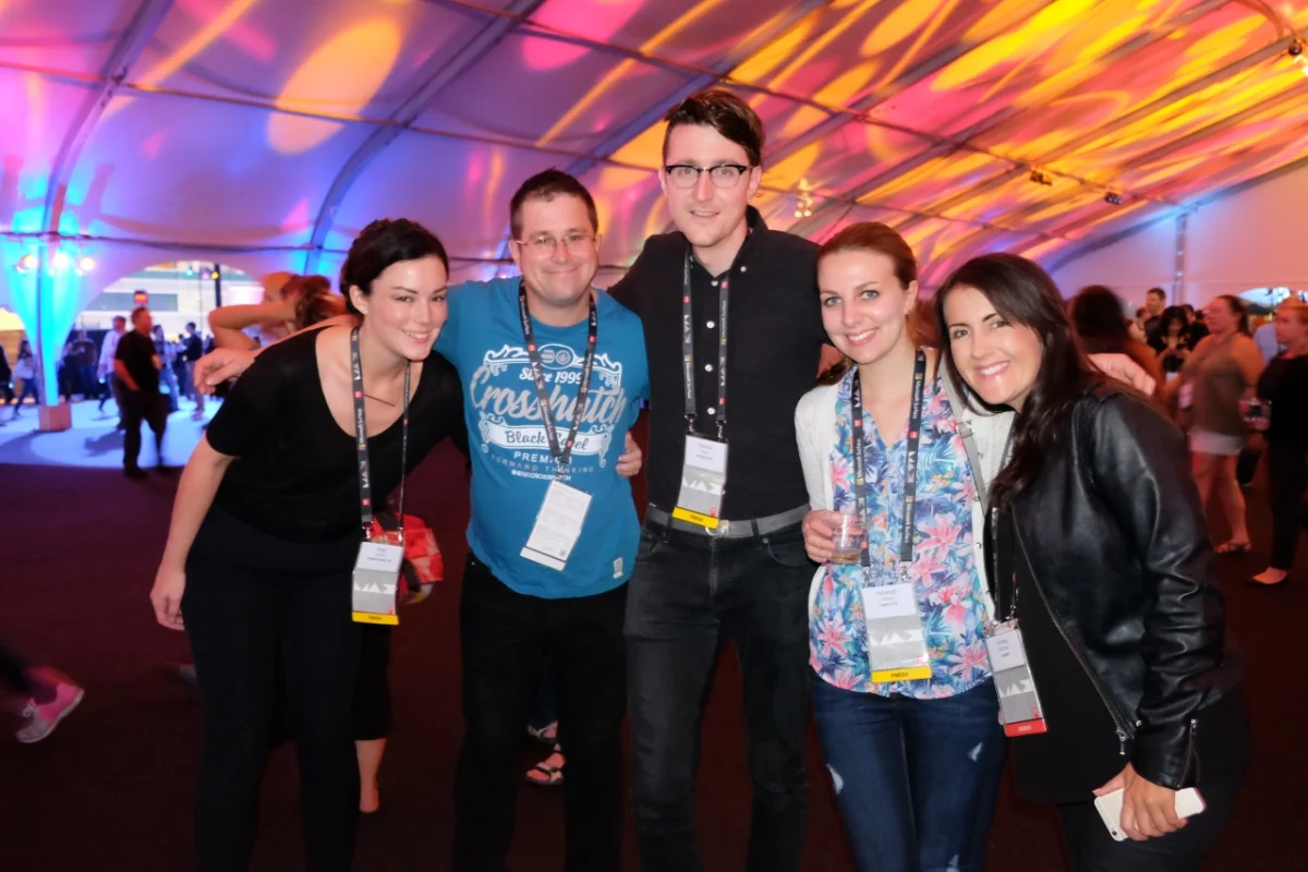 Five people wearing conference lanyards pose together under colourful pink and yellow lighting at Adobe MAX 2015