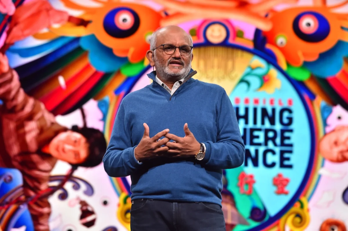 Man in blue jumper speaking in front of colourful abstract backdrop at Adobe MAX conference