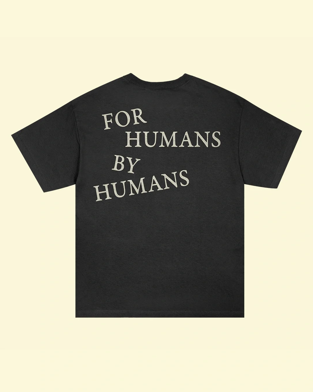 Black t-shirt printed with white text reading "FOR HUMANS BY HUMANS" on the back, displayed against a cream background