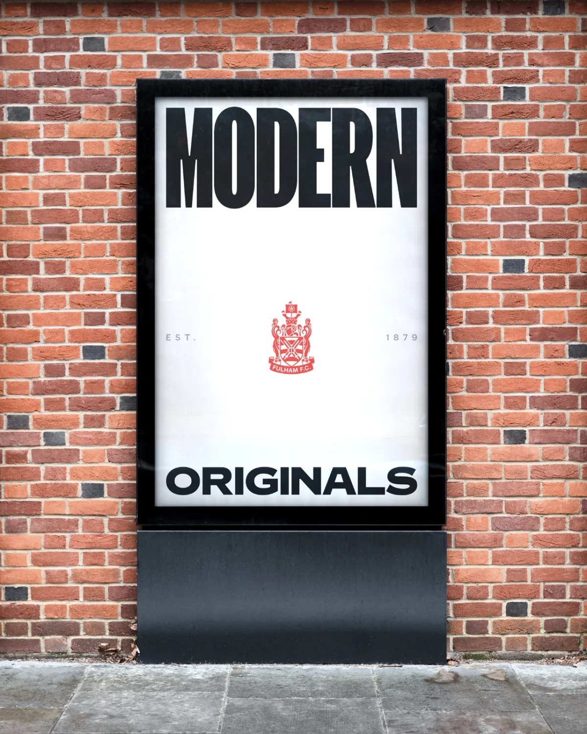 Black framed sign mounted on red brick wall reading "MODERN" at top and "ORIGINALS" at bottom with a red heraldic crest in the centre and dates either side